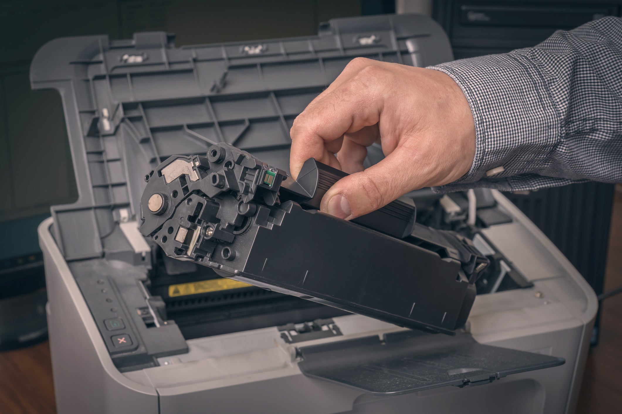 Hand installing a toner cartridge into a printer, showing services from a remanufactured toner supplier for green printing.