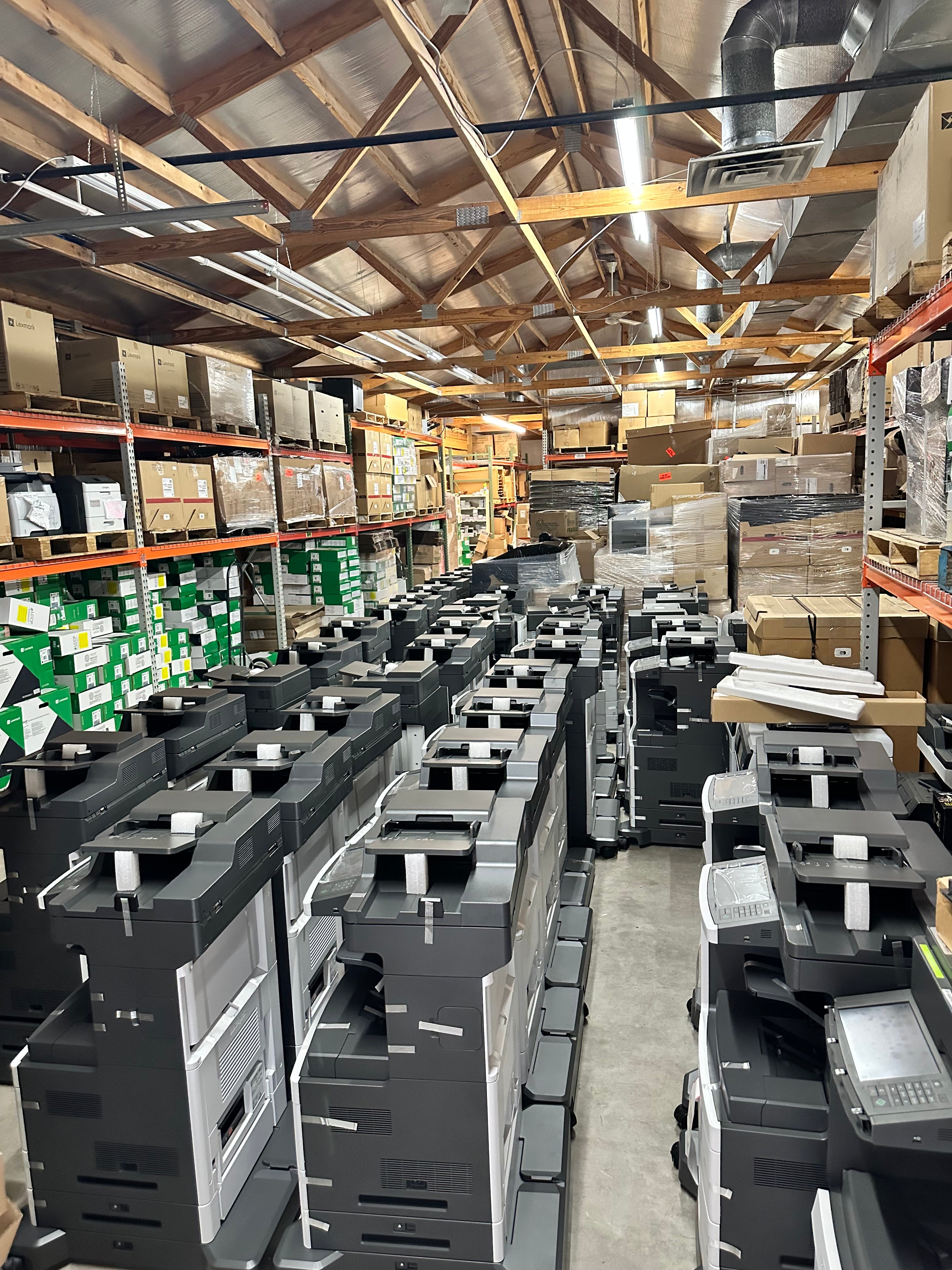 Warehouse filled with rows of printers and stacked boxes of supplies, showcasing the inventory of Impression Products.