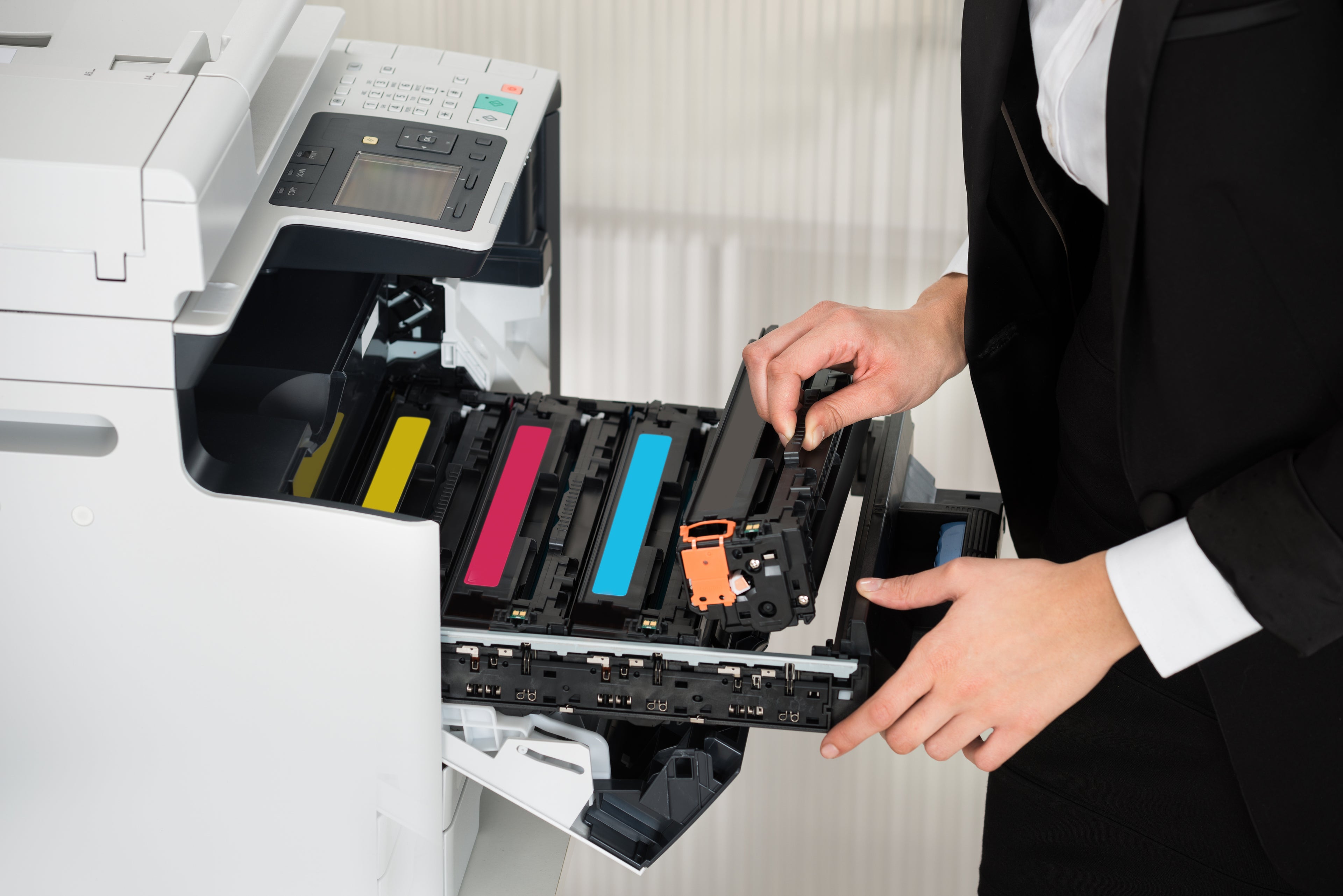 A person in business attire replacing printer cartridges in a large office copier, ensuring smooth printing operations.